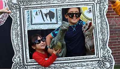 two children pose in a giant frame with plastic dinosaurs banner