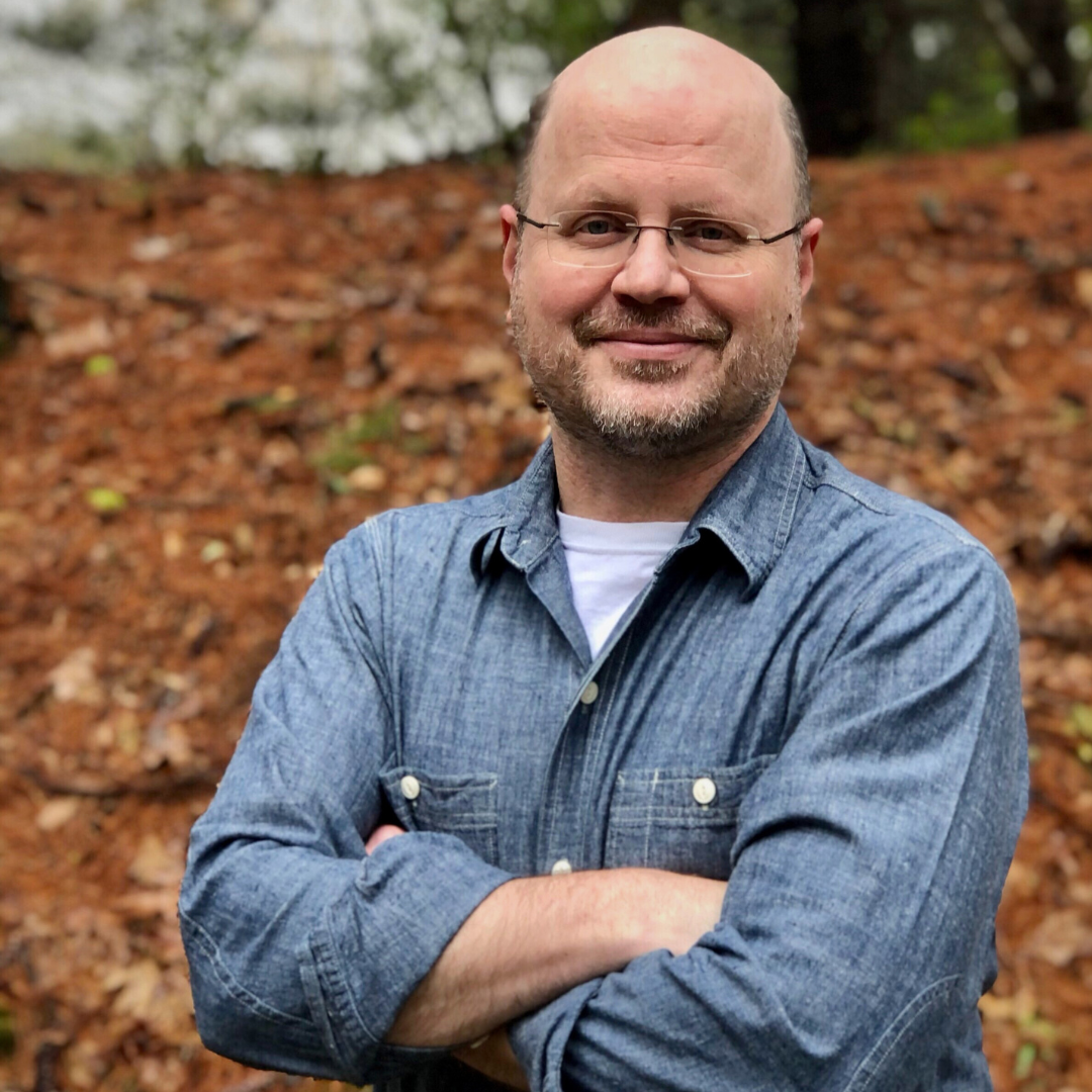 author Steve Edwards stands in forest with arms crossed